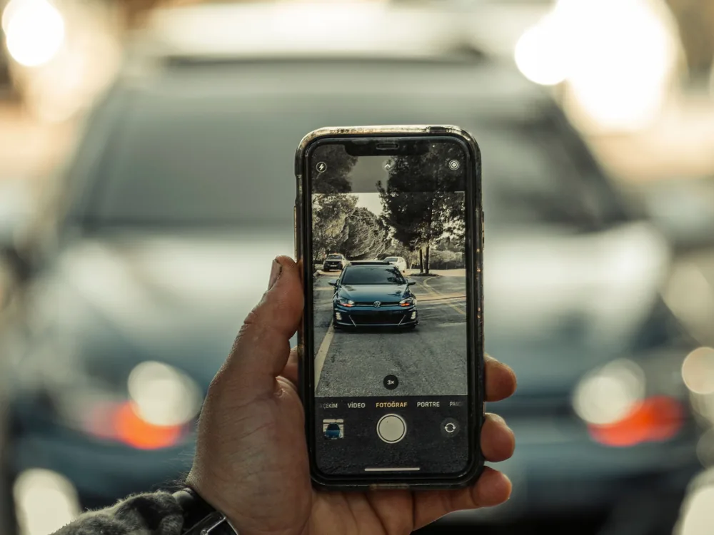Kéz mobiltelefonnal fényképez egy parkoló autót, a kijelzőn az autó képe látszik
