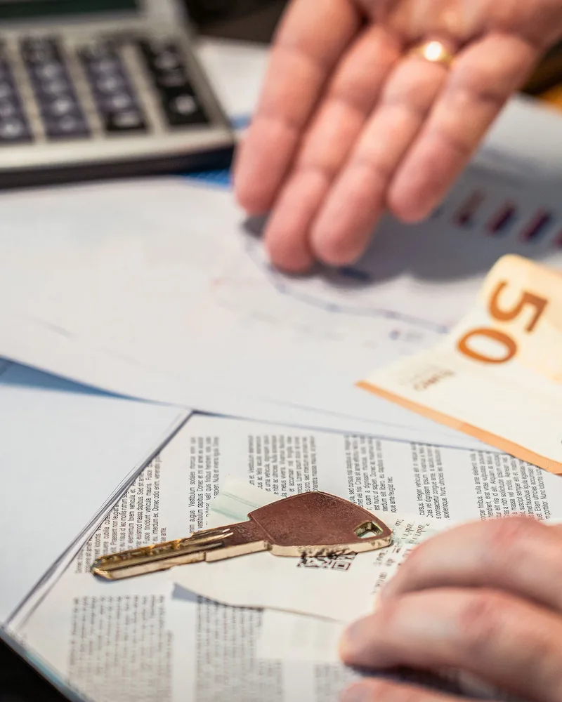 Asztalon kiterített autós okmányok, egy ötveneurós bankjegy és egy autókulcs, fölöttük egy idősebb ember keze